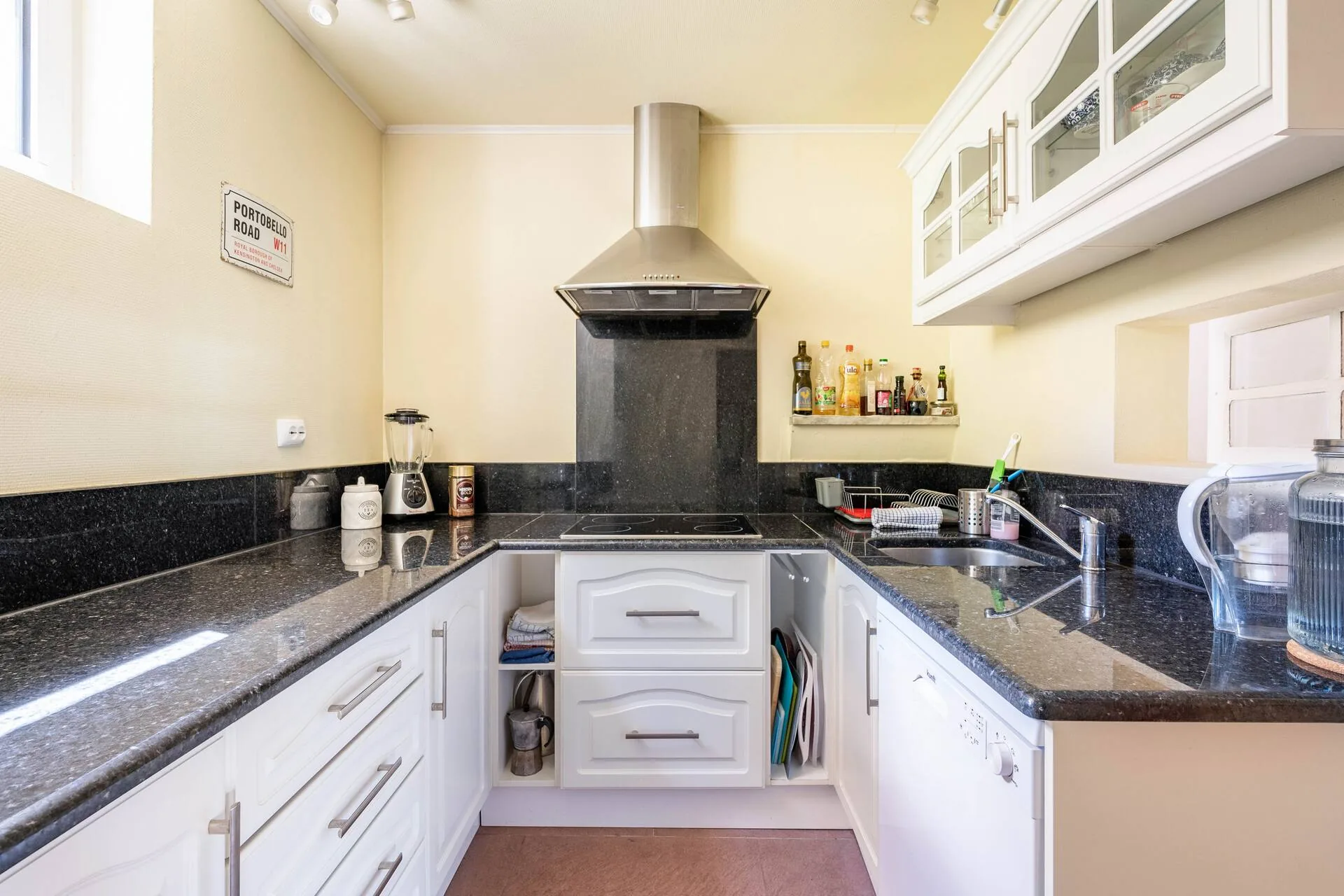 Kitchen with black granite worktops, cream cabinets, an induction hob under a stainless steel extractor, and a dishwasher.