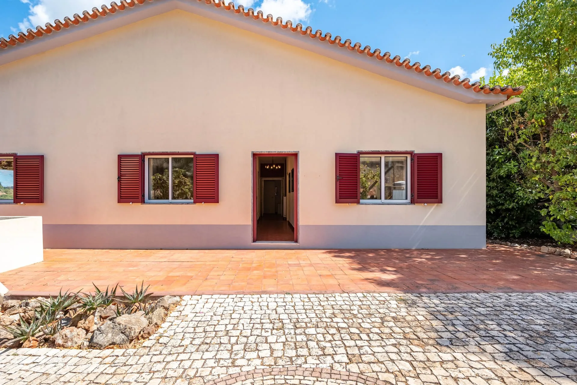 The front of the villa: cream walls, a terracotta tiled roof, deep red shutters and a cobbled driveway.