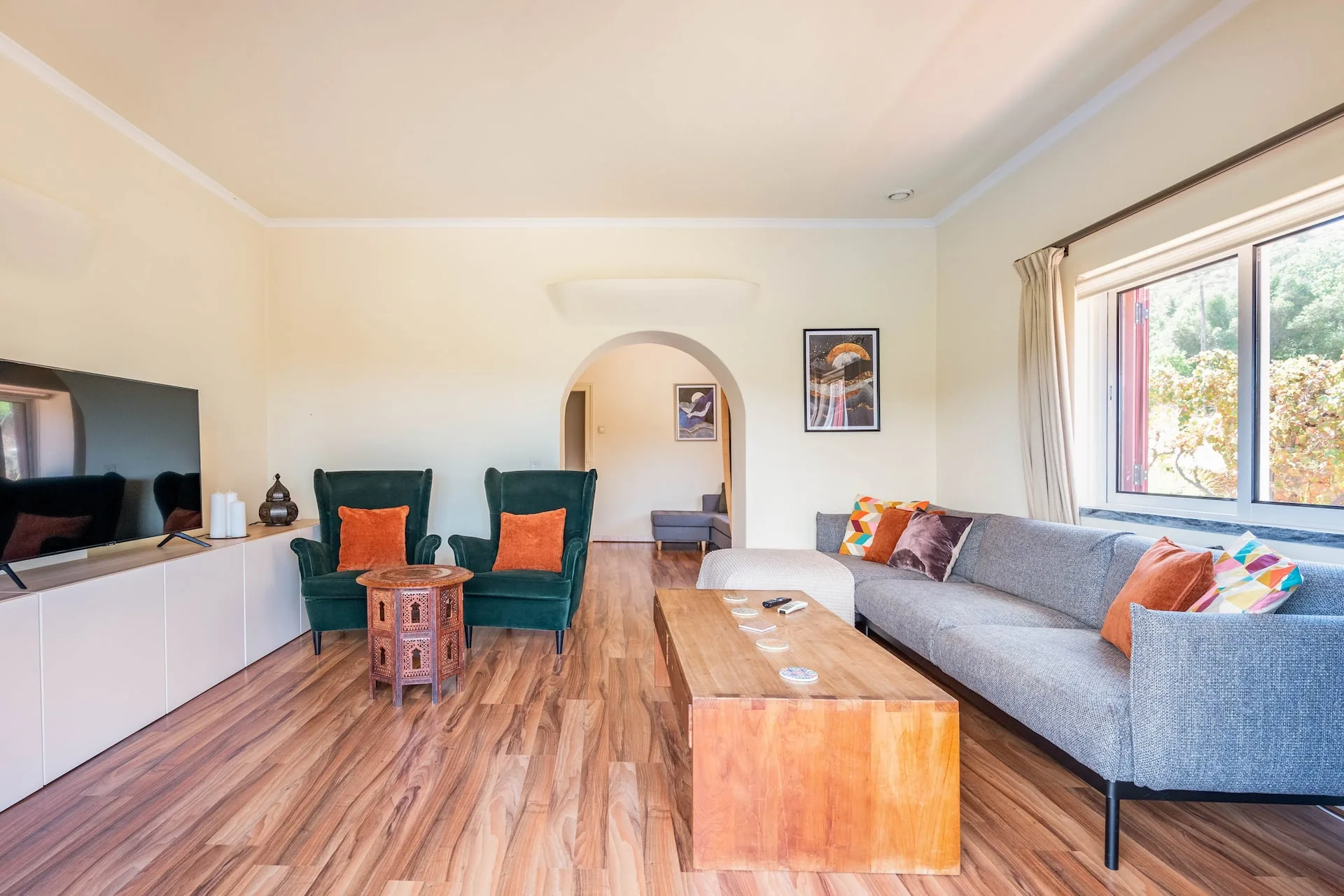 Open-plan sitting room with green velvet armchairs, a large wall-mounted TV and an archway through to a second seating area.